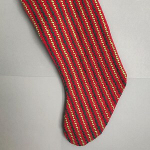 May include: Red Christmas stocking with green and gold stripes. The stocking is hanging from a green ribbon.