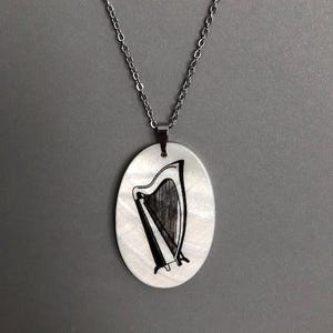 May include: A silver chain necklace with an oval-shaped mother-of-pearl pendant featuring a black and white illustration of a harp.