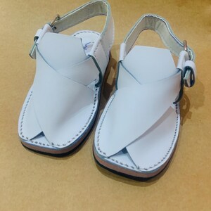 May include: A pair of white leather sandals with a cross-strap design. The sandals have a light blue trim and a buckle closure. The soles are brown and black. The sandals are designed for children.