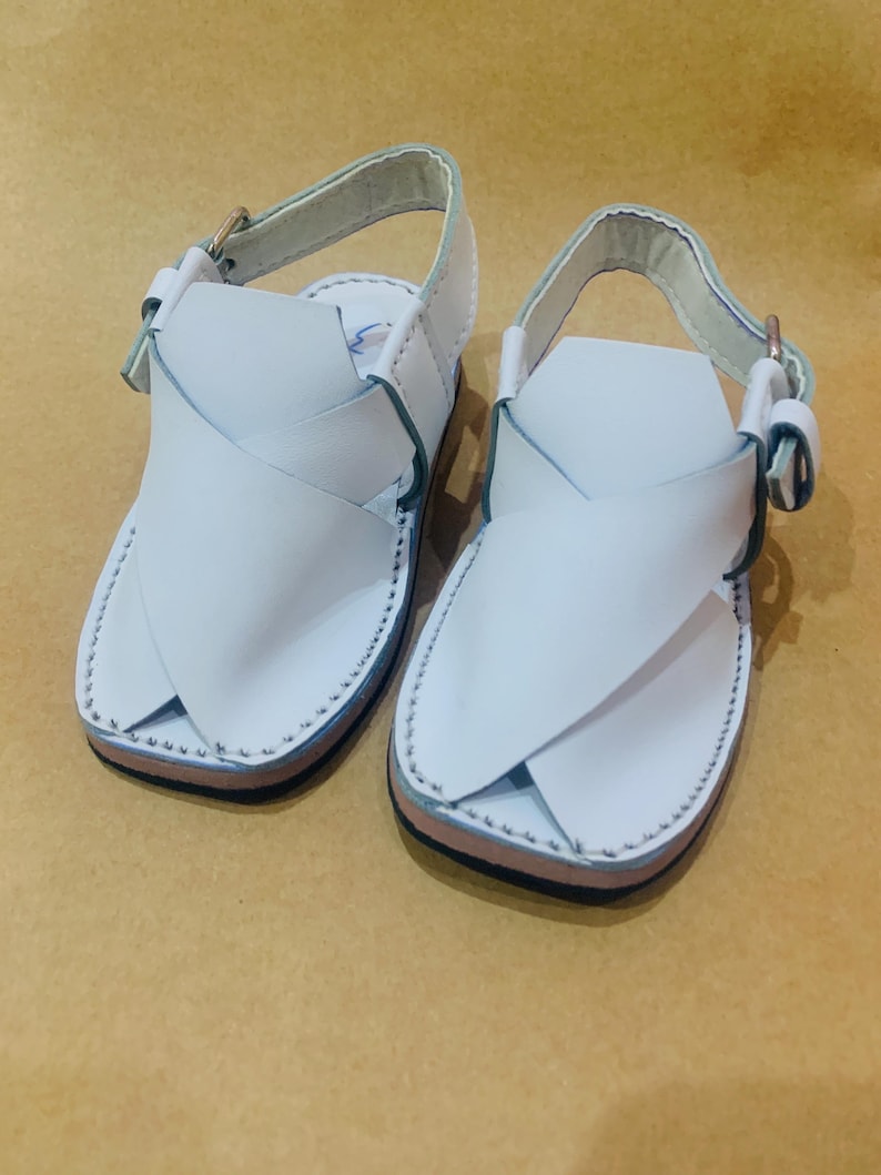 May include: A pair of white leather sandals with a cross-strap design. The sandals have a light blue trim and a buckle closure. The soles are brown and black. The sandals are designed for children.