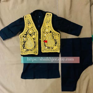 May include: A black outfit featuring a vest with gold embroidery and mirror accents, a long-sleeved shirt, and matching pants. The vest has a decorative design and a red tassel. The outfit is likely for a special occasion.