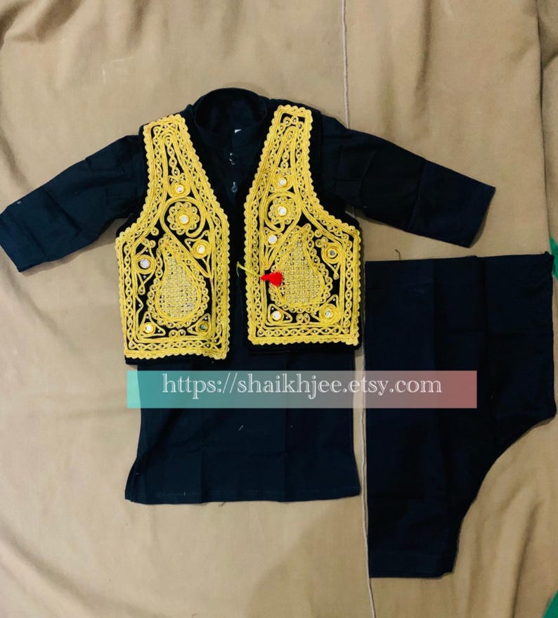 May include: A black outfit featuring a vest with gold embroidery and mirror accents, a long-sleeved shirt, and matching pants. The vest has a decorative design and a red tassel. The outfit is likely for a special occasion.