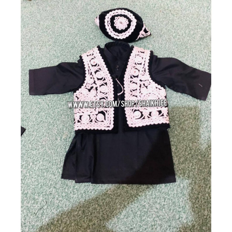 May include: A black outfit for a child, including a long-sleeved shirt, vest, and cap. The vest and cap feature white, intricate lace-like detailing. The outfit is displayed on a light green surface. The text "WWW.ETSY.COM/SHOP/SHAIKHJEE" is visible.