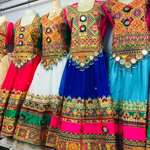 May include: A display of embroidered dresses in various colours, including red, white, blue, and green. The dresses are adorned with intricate patterns and mirror embellishments. They are hanging on a metal rail.