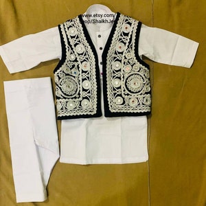 May include: A white kurta pajama set with a black vest. The vest is adorned with intricate silver embroidery and small, reflective mirror accents. The outfit is designed for children and is displayed on a golden-brown surface. The text "www.etsy.com/shop/ShaikhJee" is visible.