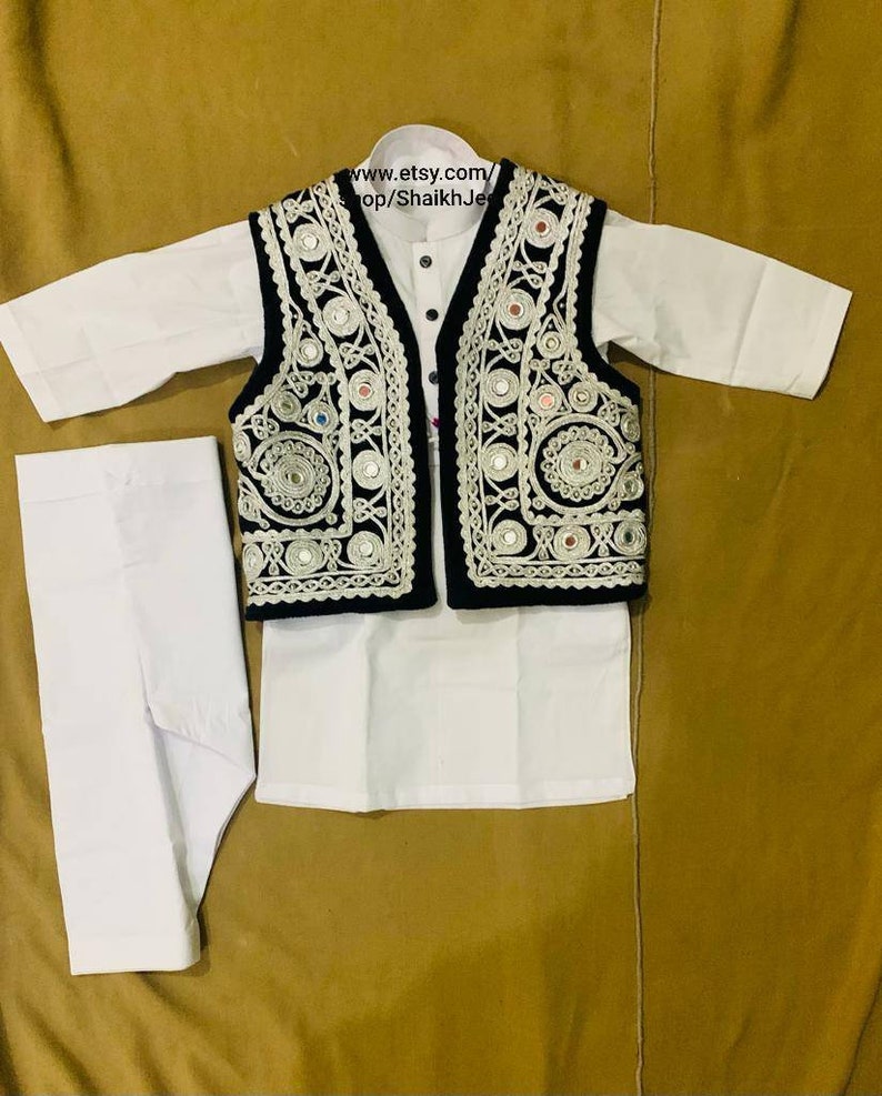 May include: A white kurta pajama set with a black vest. The vest is adorned with intricate silver embroidery and small, reflective mirror accents. The outfit is designed for children and is displayed on a golden-brown surface. The text "www.etsy.com/shop/ShaikhJee" is visible.