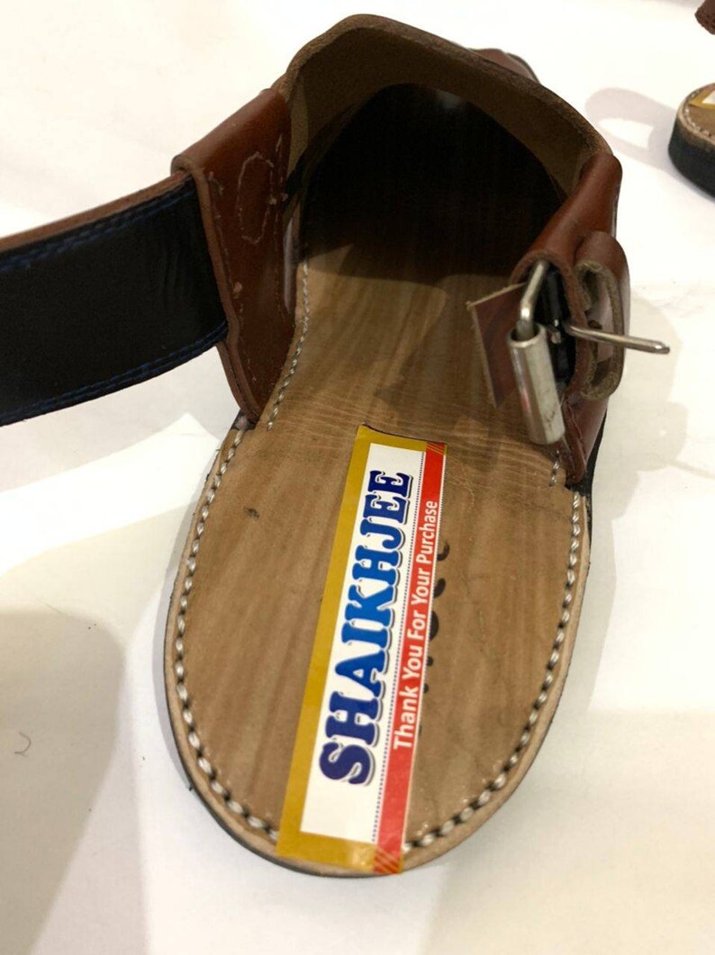 K&ouml;nnte beinhalten: Nahaufnahme einer braunen Ledersandale mit Schnallenverschluss. Die Sandale hat eine hellbraune Innensohle mit einer gen&auml;hten Bord&uuml;re. Ein Aufkleber mit dem Text "SHAIKHJEE Thank You For Your Purchase" ist sichtbar.