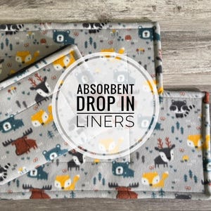 May include: Gray absorbent drop-in liners with a woodland animal pattern. The pattern includes bears, foxes, deer, and raccoons. The liners have a quilted design and are bordered with a contrasting color.