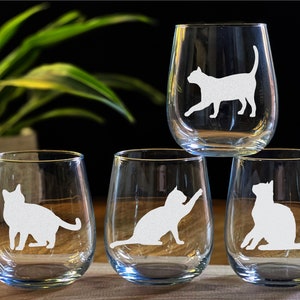 May include: Four clear glass wine glasses with white cat silhouettes etched on them. The glasses are stacked on top of each other.