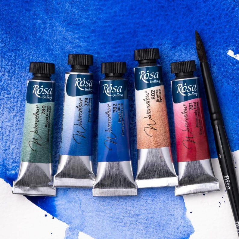 May include: Five tubes of Rosa Gallery watercolor paint in the colors Royal Green, Prussian Blue, Cerulean Blue, Bronze, and Burgundy Red. The tubes are arranged in a row on a blue background.