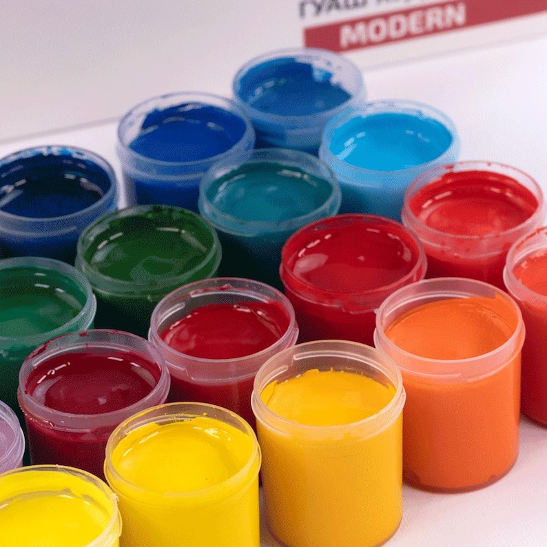 May include: Assortment of paint pots in various colors, including red, blue, green, yellow, and orange. The paint pots are arranged in a semi-circle on a white surface.