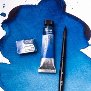 May include: Two tubes of Rosa Gallery watercolor paint in Prussian Blue, one in a tube and one in a pan, with a black paintbrush.