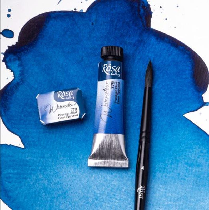 May include: Two tubes of Rosa Gallery watercolor paint in Prussian Blue, one in a tube and one in a pan, with a black paintbrush.