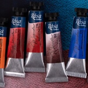 May include: Ten tubes of watercolor paint in various colors, labeled "R&oacute;sa Gallery Watercolor" with different numbers. The tubes are arranged in a row on a textured surface.