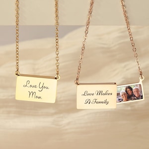 May include: Two gold necklaces with rectangular pendants. One pendant says "Love You Mom" and the other says "Love Makes A Family" and has a small photo of a family inside.