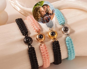 May include: Four friendship bracelets in black, pink, and blue, each featuring a central sphere and woven cord design. A small circular image of a couple is superimposed on the bracelets. The bracelets are displayed on a soft, cream-colored fabric.