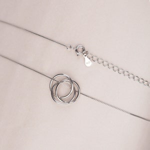 May include: A silver necklace with a delicate chain and a pendant featuring three interlocking circles.