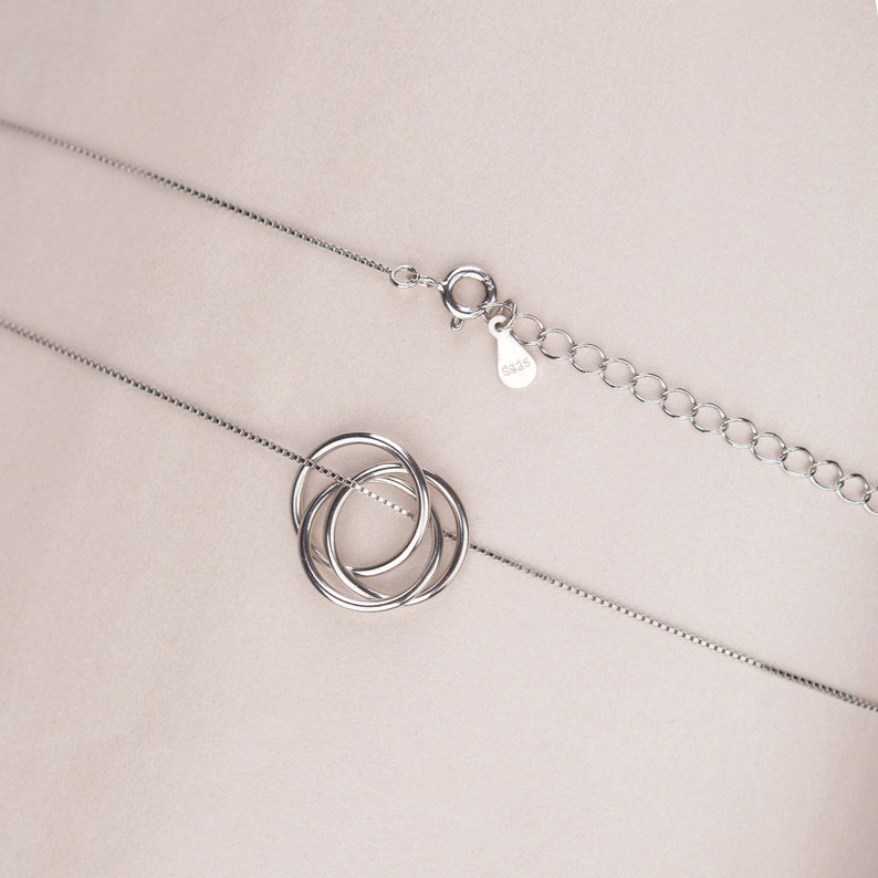 May include: A silver necklace with a delicate chain and a pendant featuring three interlocking circles.