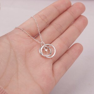 May include: A silver necklace with a delicate chain and a pendant featuring two interlocking circles with a small, clear gemstone in the center.