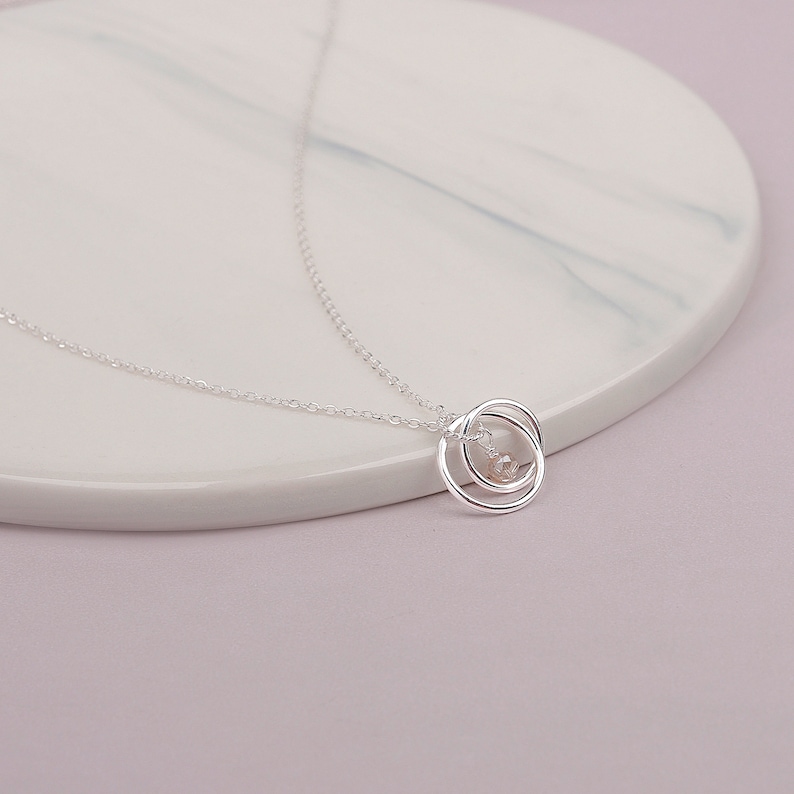 May include: A silver necklace with a delicate pendant featuring two interlocking circles. The circles are open and have a small, clear crystal in the center.