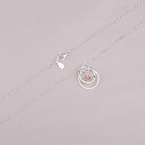 May include: A silver chain necklace with a pendant featuring two interlocking circles and a small, clear crystal in the center.
