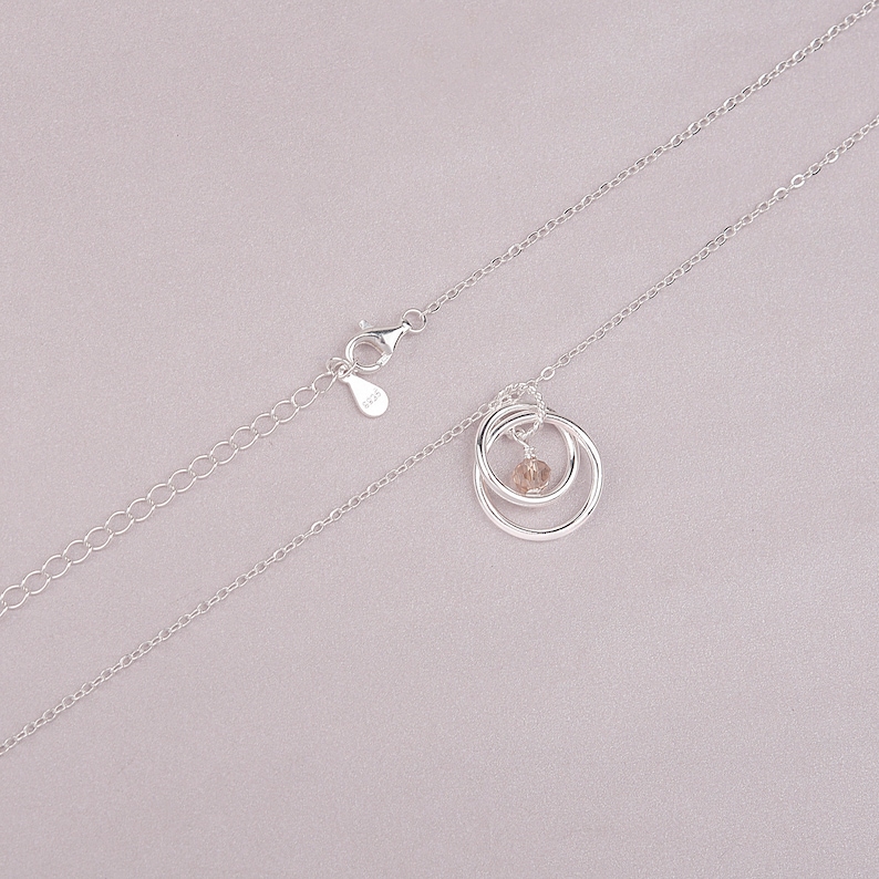 May include: A silver chain necklace with a pendant featuring two interlocking circles and a small, clear crystal in the center.