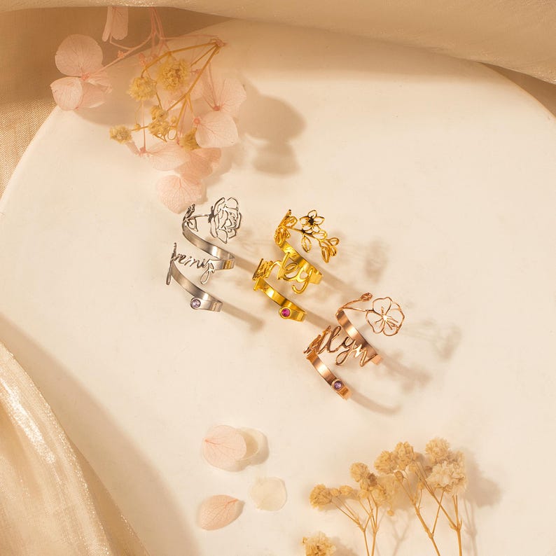 Puede incluir: Tres anillos de oro con delicados dise&ntilde;os florales y las palabras "always", "forever" y "being" inscritas en ellos. Cada anillo presenta una peque&ntilde;a piedra preciosa rosa.
