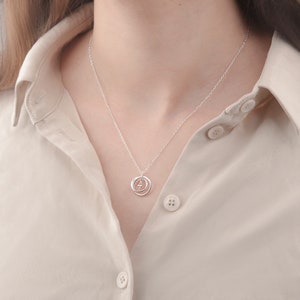 May include: A silver necklace with a delicate pendant featuring two interlocking circles and a small, clear gemstone in the center.