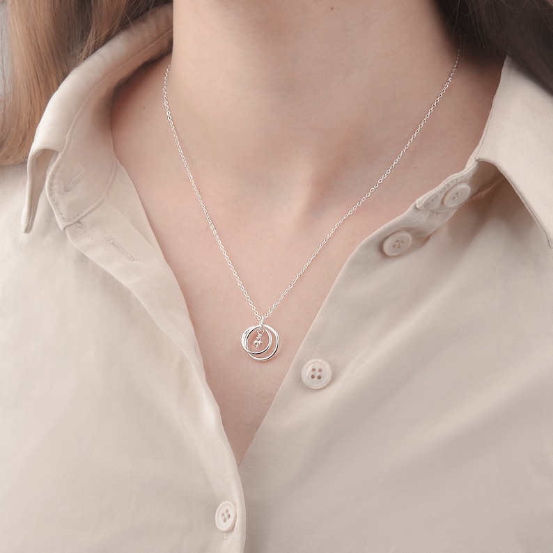 May include: A silver necklace with a delicate pendant featuring two interlocking circles and a small, clear gemstone in the center.