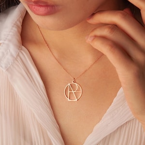 May include: A rose gold necklace with a geometric pendant featuring the letters "A" and "R" intertwined within a circle.