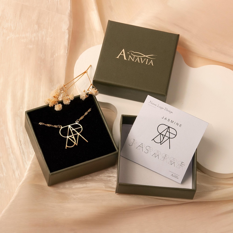 May include: A gold necklace with a custom name design in a green box. The box has the name "Anavia" printed on the top. The necklace is in a smaller box with the name "Jasmine" printed on the top.