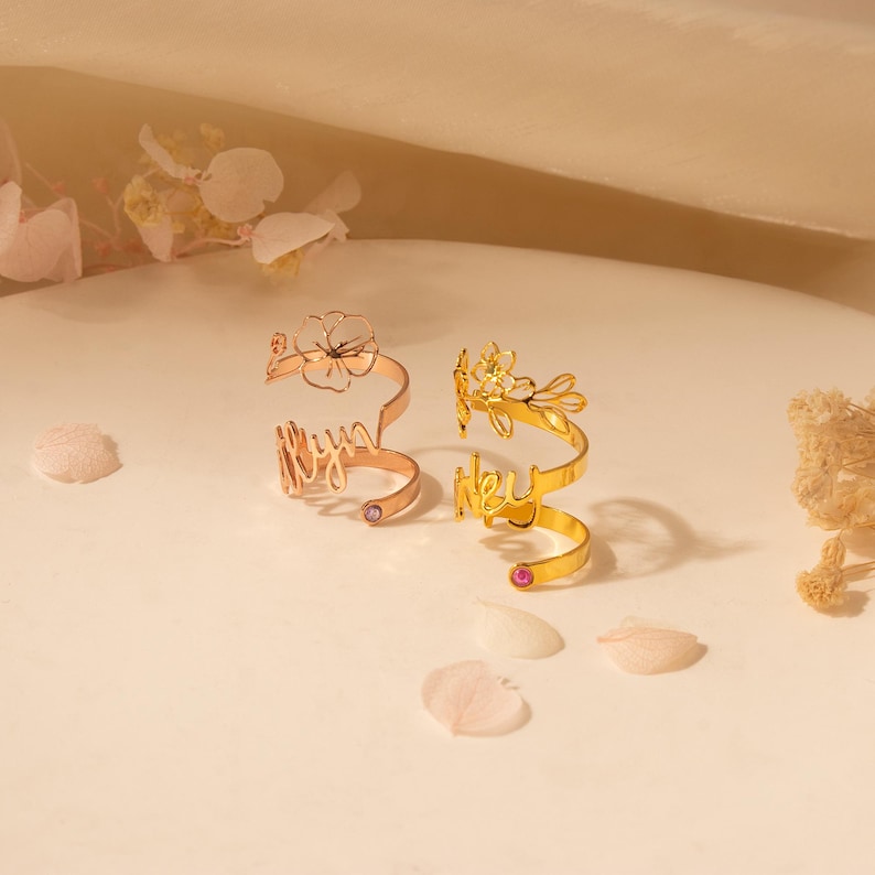 Puede incluir: Dos anillos de oro con delicados dise&ntilde;os florales y los nombres "Lily" y "Lexi" inscritos en ellos. Cada anillo tiene una peque&ntilde;a piedra preciosa rosa.