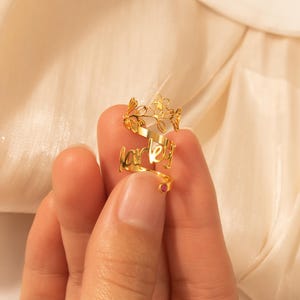 Puede incluir: Anillo de oro con el nombre "Harley" escrito en cursiva. El anillo est&aacute; adornado con un delicado dise&ntilde;o floral y una peque&ntilde;a piedra preciosa rosa.