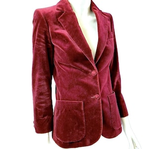 May include: A burgundy velvet blazer with a single-button closure and two front pockets. The blazer has a classic notched lapel and long sleeves. The fabric has a soft, luxurious texture.