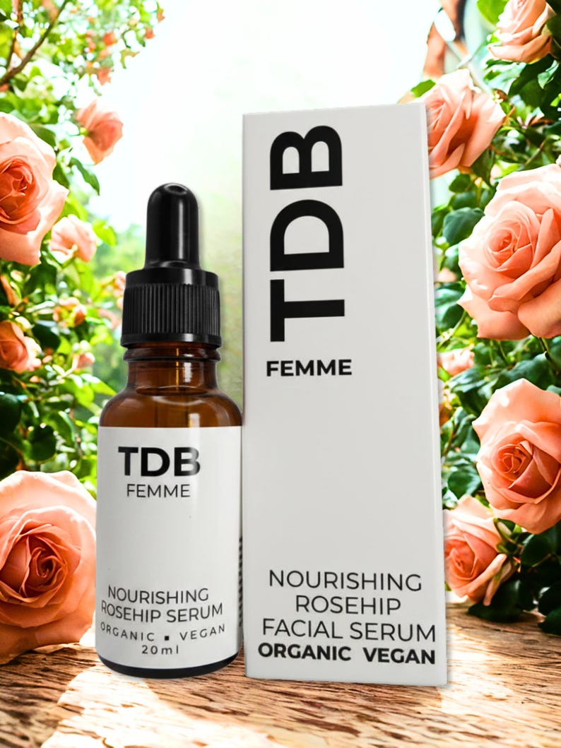 May include: A brown glass bottle with a black dropper and a white label, next to a white box. Both feature the text "TDB FEMME" and product details. The bottle contains 20 ml of Nourishing Rosehip Serum, and the box describes it as an Organic Vegan Facial Serum.