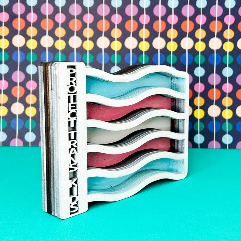 May include: A wooden cutout of a transgender pride flag with the words "Protect Trans Kids" on the side. The flag is made of multiple layers of wood, each painted a different color. The colors of the flag are light blue, white, pink, and light blue.