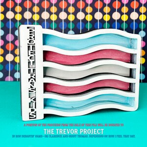 May include: A white wooden flag with wavy stripes in blue, pink, and gray. The flag is attached to a wooden post with the text "PROJECT TRANS KIDS" printed on it. A portion of the proceeds from the sale of this file will be donated to The Trevor Project.