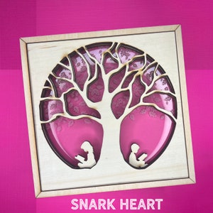 May include: A wooden box with a cutout of a tree with two figures sitting beneath it reading. The tree is surrounded by a pink background. The box has the words "SNARK HEART" printed on the bottom.