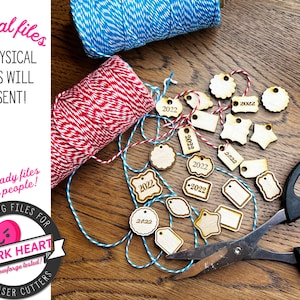 May include: A collection of laser-cut wooden tags with the year 2022 inscribed on them. The tags are arranged on a wooden surface with red and blue twine. The image also includes a pair of scissors and a digital file logo with the text "Digital SVG Files for Snark Heart Glowforge tested! Laser Cutters".