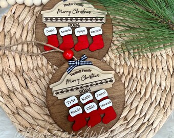 May include: Two wooden Christmas ornaments with the text "Merry Christmas" and the year "2024". The ornaments are decorated with red and white stockings and have the names of family members written on them.
