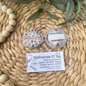 May include: A clear plastic stethoscope ID tag with a silver and pink design that says "Gilkies. RN". The tag snaps onto the stethoscope tubing and has a write-on surface on the back. The tag is labeled "Stethoscope ID Tag" and has the product number 250040.