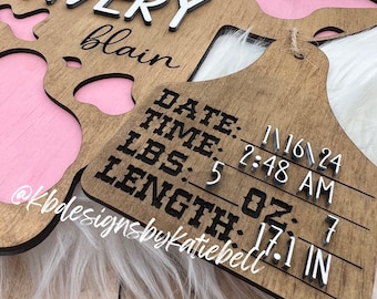 Könnte beinhalten: Ein hölzernes Schild in Kuhform mit einem rosa Ausschnitt in Form eines Kuhflecks. Das Schild trägt den Namen Avery blain, das Datum 16.11.24, die Uhrzeit 2:48 Uhr, das Gewicht 5 oz und die Länge 17,1 in.