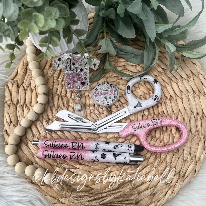 May include: Pink and white glitter nurse themed retractable badge reel with a pair of pink scissors with the text "Silkies RN" and two pink pens with the text "Silkies RN".