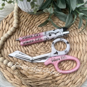 May include: Two pink and white glitter pens with the text "Silkies. RN" and a pair of pink and white glitter medical scissors with the text "Silkies. RN".