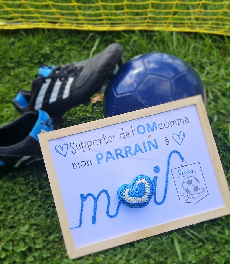 May include: A framed sign with a blue crocheted heart and the text "Supporter de l'OM comme mon PARRAIN &agrave;" and "Lucas 27 juin 2019".