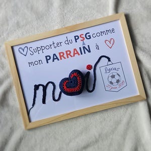 May include: A framed white board with the text "Supporter du PSG comme mon PARRAIN &agrave;" and a blue and red crocheted heart with the word "moi" written in blue yarn. The board also has a small white card with the text "Lucas 27 juin 2019" and a soccer ball graphic.