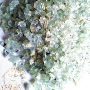 May include: A close-up of iridescent green and blue glass glitter. The glitter is made of small, irregular pieces of glass that sparkle in the light.