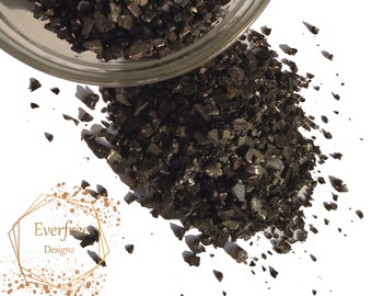 May include: A glass bowl filled with black iridescent glass shards. The bowl is tipped over, spilling the shards onto a white surface.