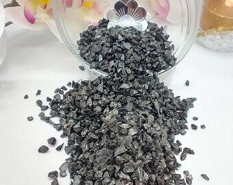 May include: A close-up of a bowl filled with black crushed glass, with some of the glass spilling out onto a white surface.