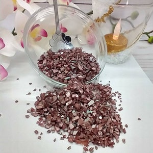 May include: A glass bowl filled with iridescent rose gold glass chips. The chips are scattered on a white surface.